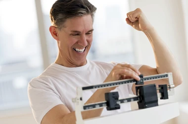 A man celebrating results while he weighs himself on a scale
